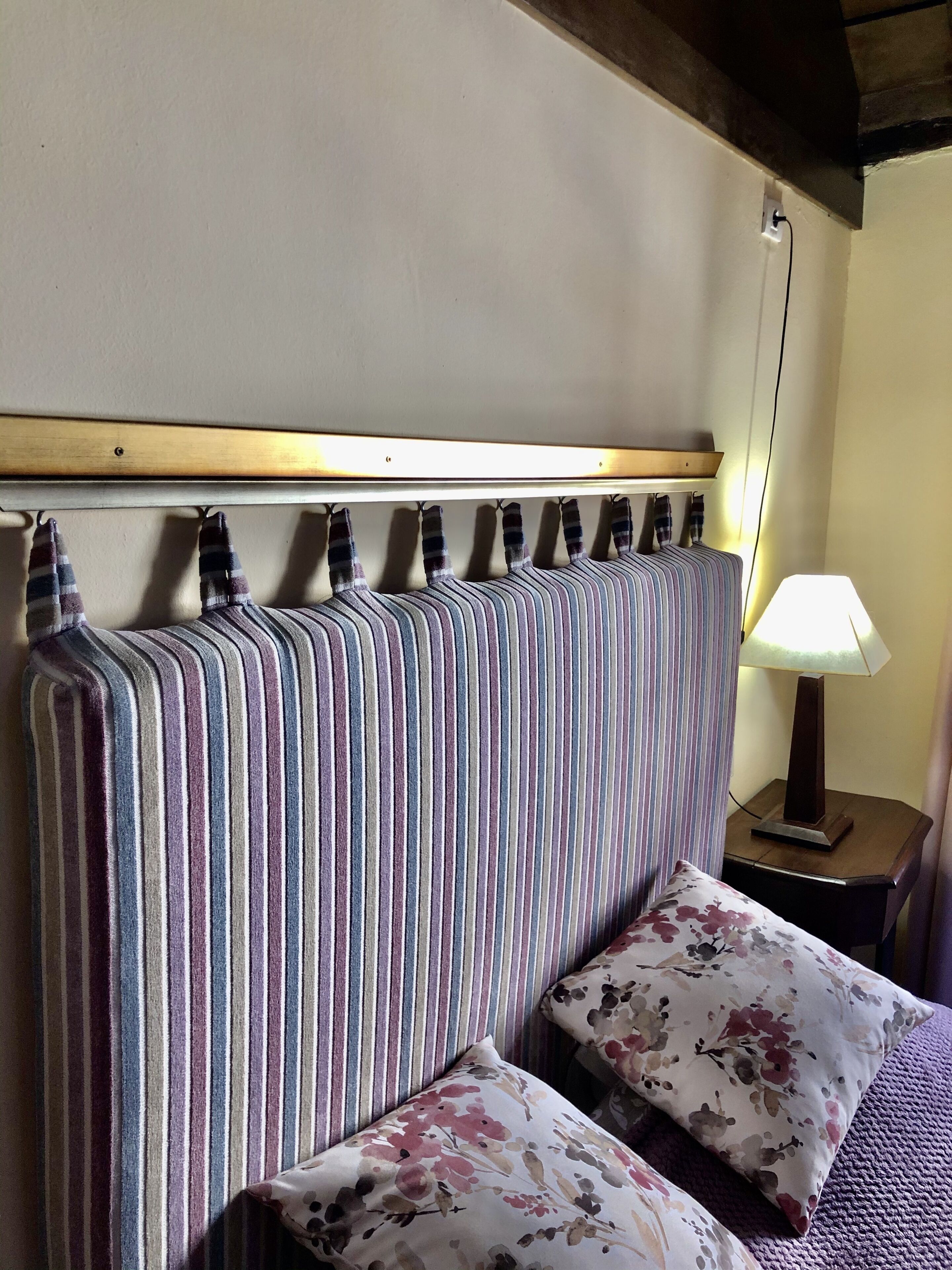 A room with a striped headboard, a floral pillow, and a bedside lamp.