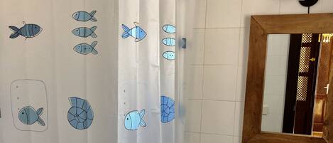 Un baño con cortina de ducha estampada con motivos de peces, un lavamanos y un espejo.