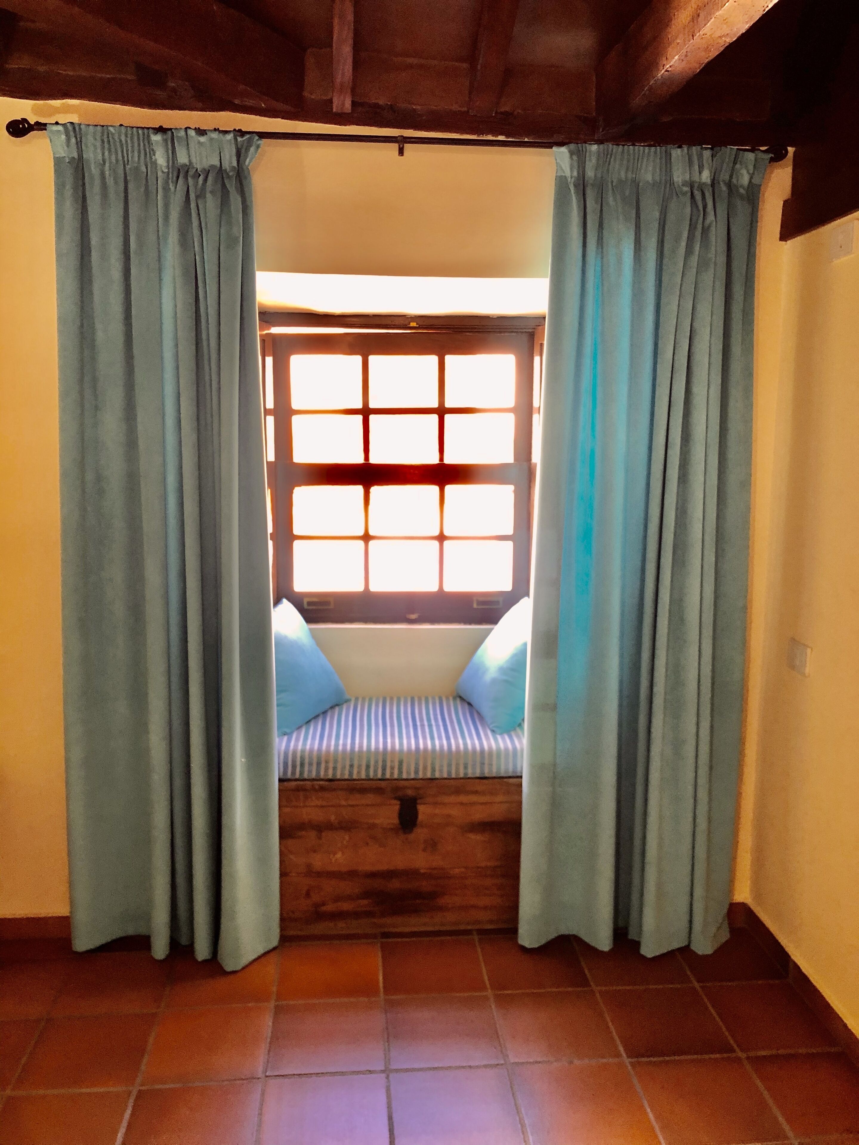 A room with a window, curtains, a bench, and a tiled floor.