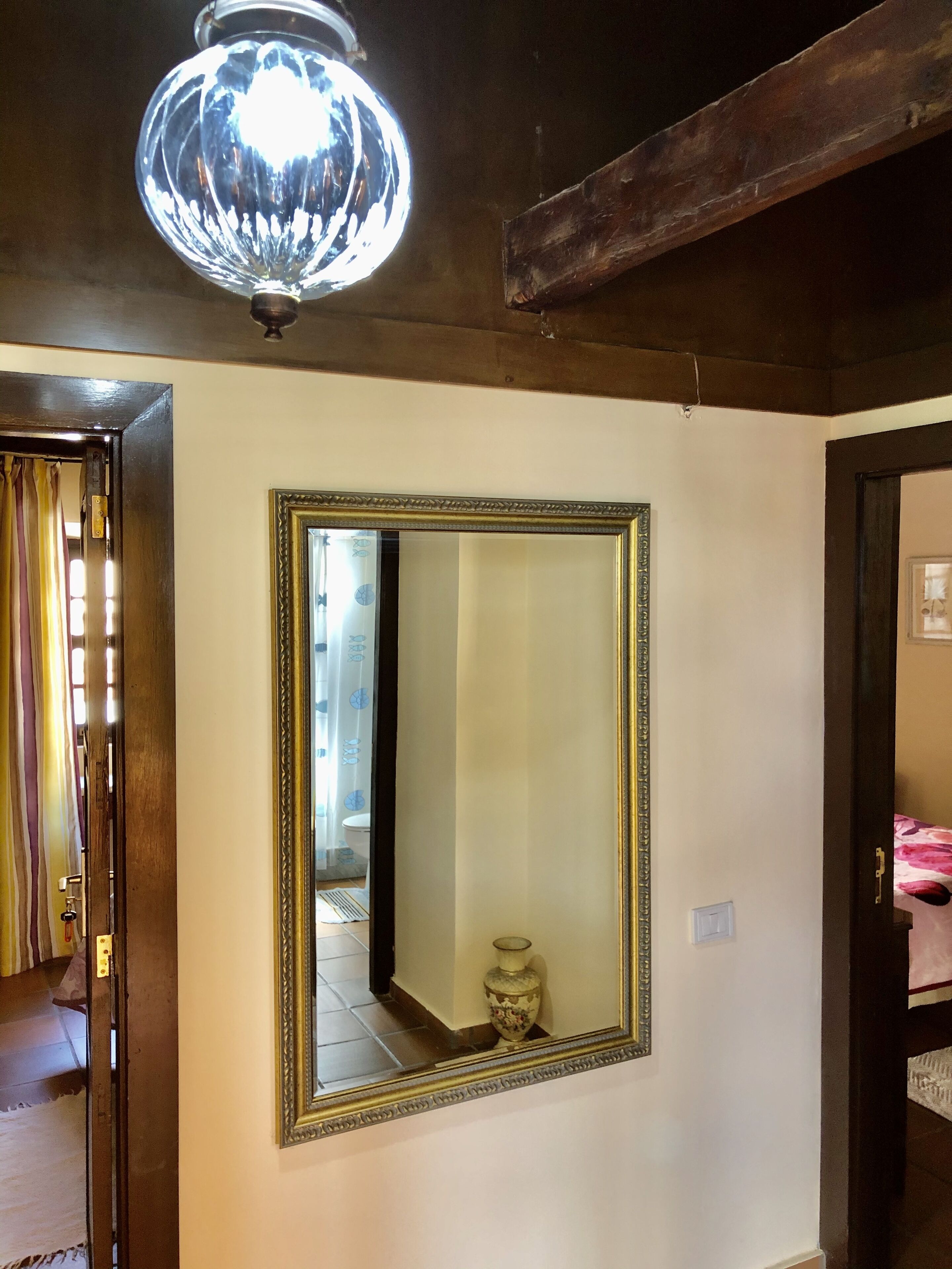 Una habitación con un espejo grande en la pared, una viga de techo de madera y una lámpara colgante.