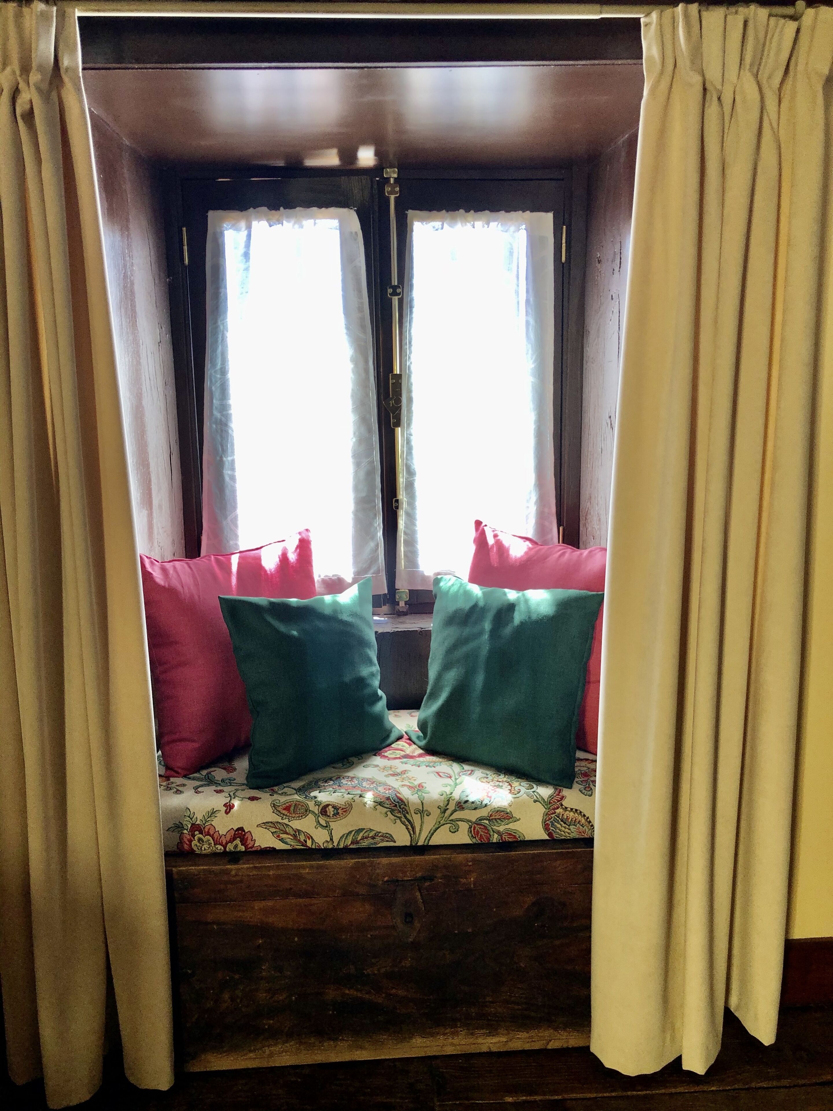 A cozy cabin with a wooden bench, two windows with curtains, and a view of the outdoors.