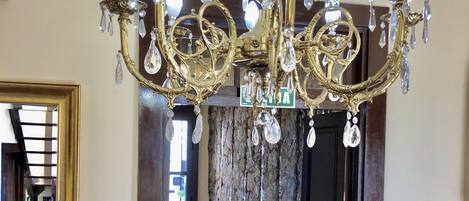 Un couloir orné d’un lustre, d’un miroir, d’une porte sur laquelle est apposé un panneau « Interdiction de fumer » et d’une chaise à motifs.
