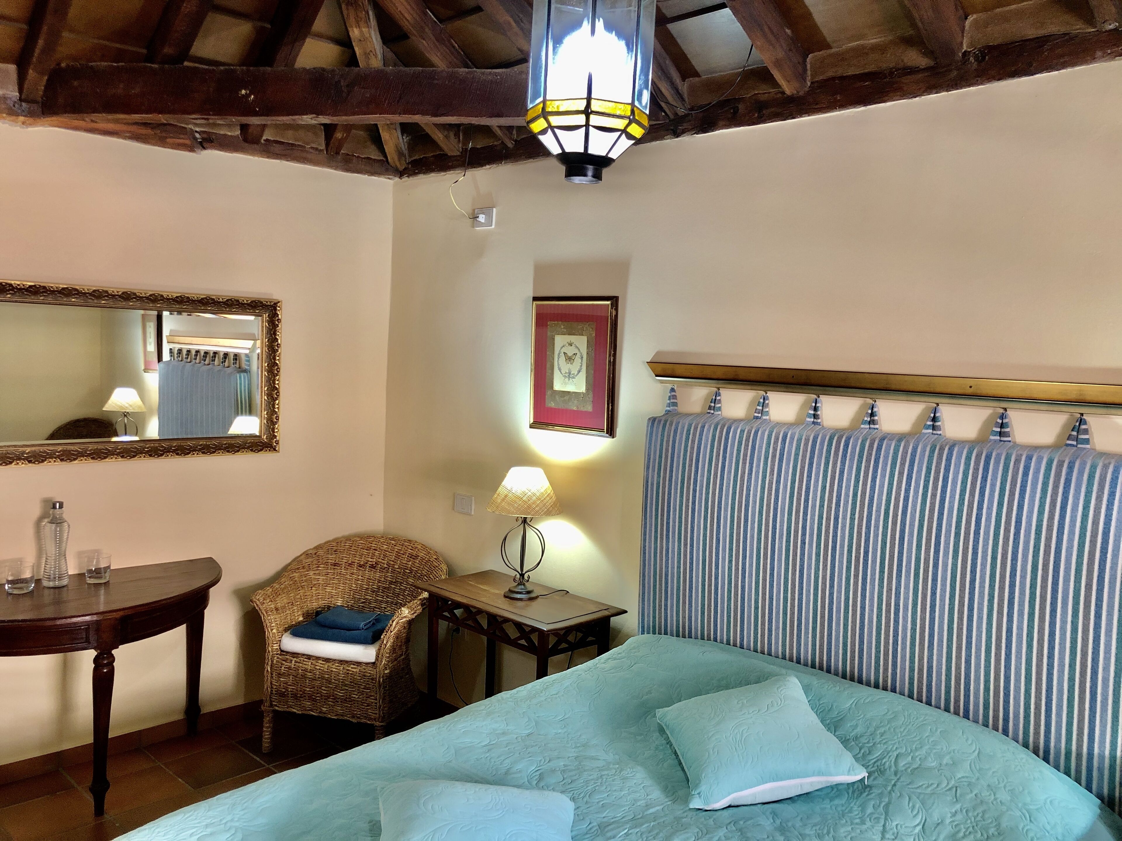 Una habitación con una cama, una silla, una mesa, una lámpara, un espejo y un cuadro en la pared.