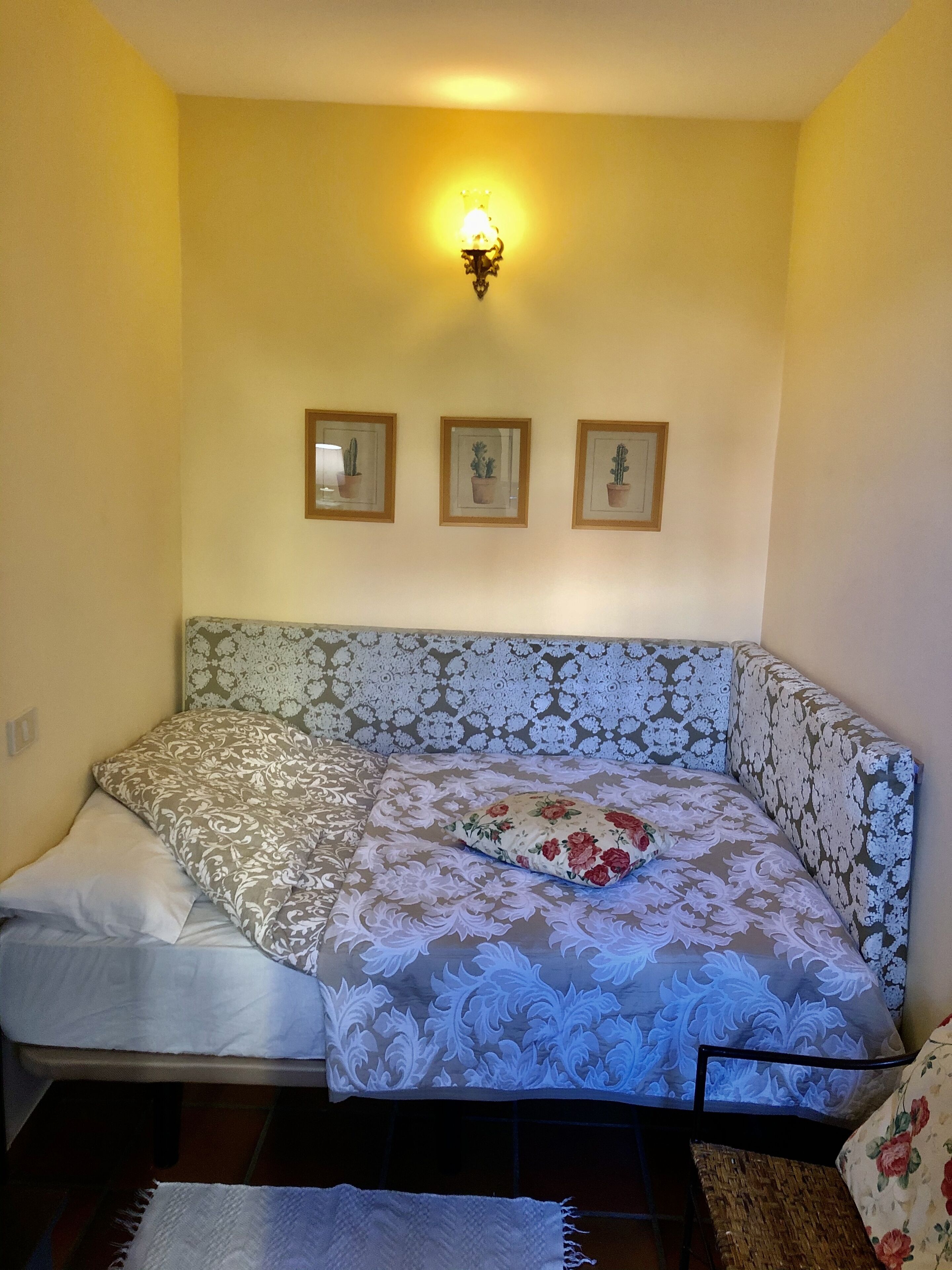 A room with a sofa bed, a wall-mounted light fixture, and three framed pictures.