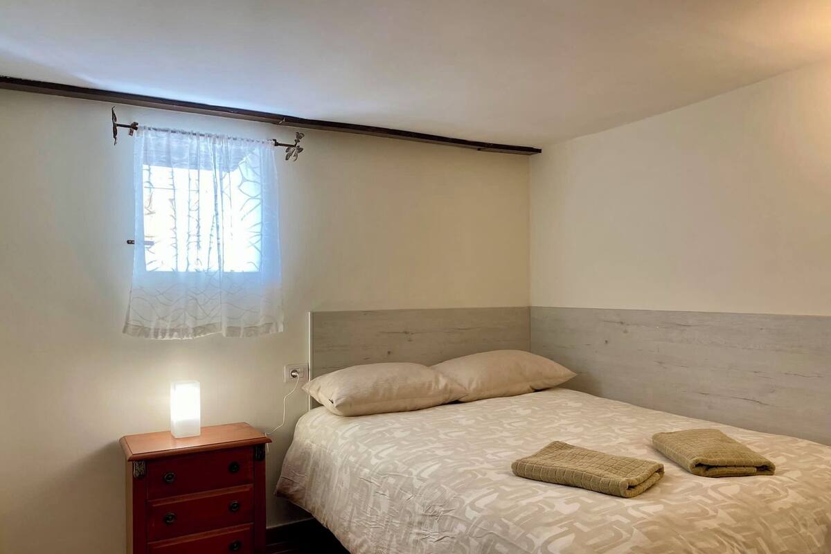 A bedroom with a bed, a nightstand, a dresser, and a window with a curtain.