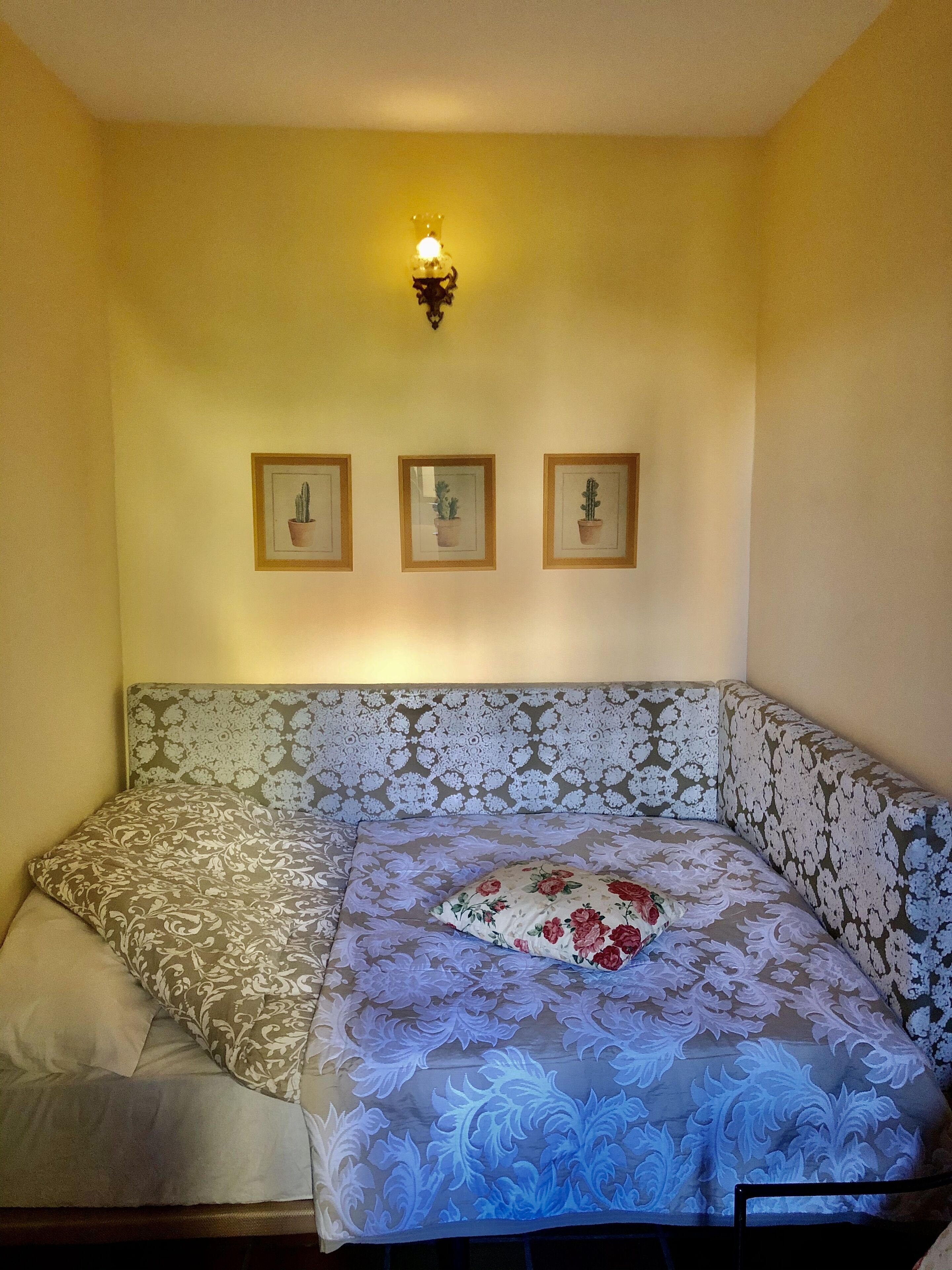 Una habitación con una cama, una lámpara fijada a la pared y tres cuadros con imágenes de cactus.