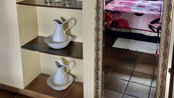 A room with a bed, a mirror, and shelves with kitchenware.