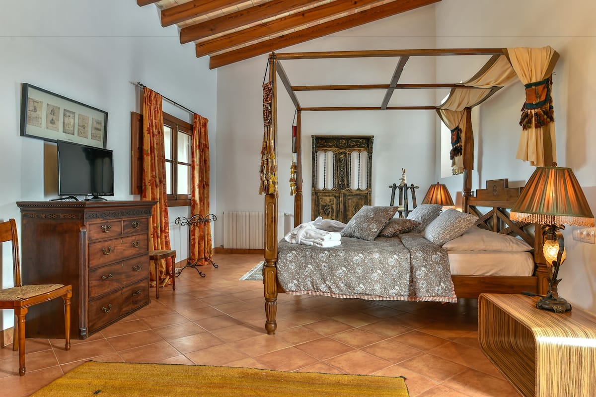 A traditional bedroom with a four-poster bed, wooden furniture, and a television on a dresser.