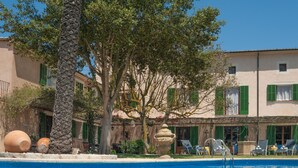 A pool area with a stone pillar, terracotta pots, and a building with green shutters. - Agroturismo Fincahotel Es Llobets - Adults Only (Llucmajor)