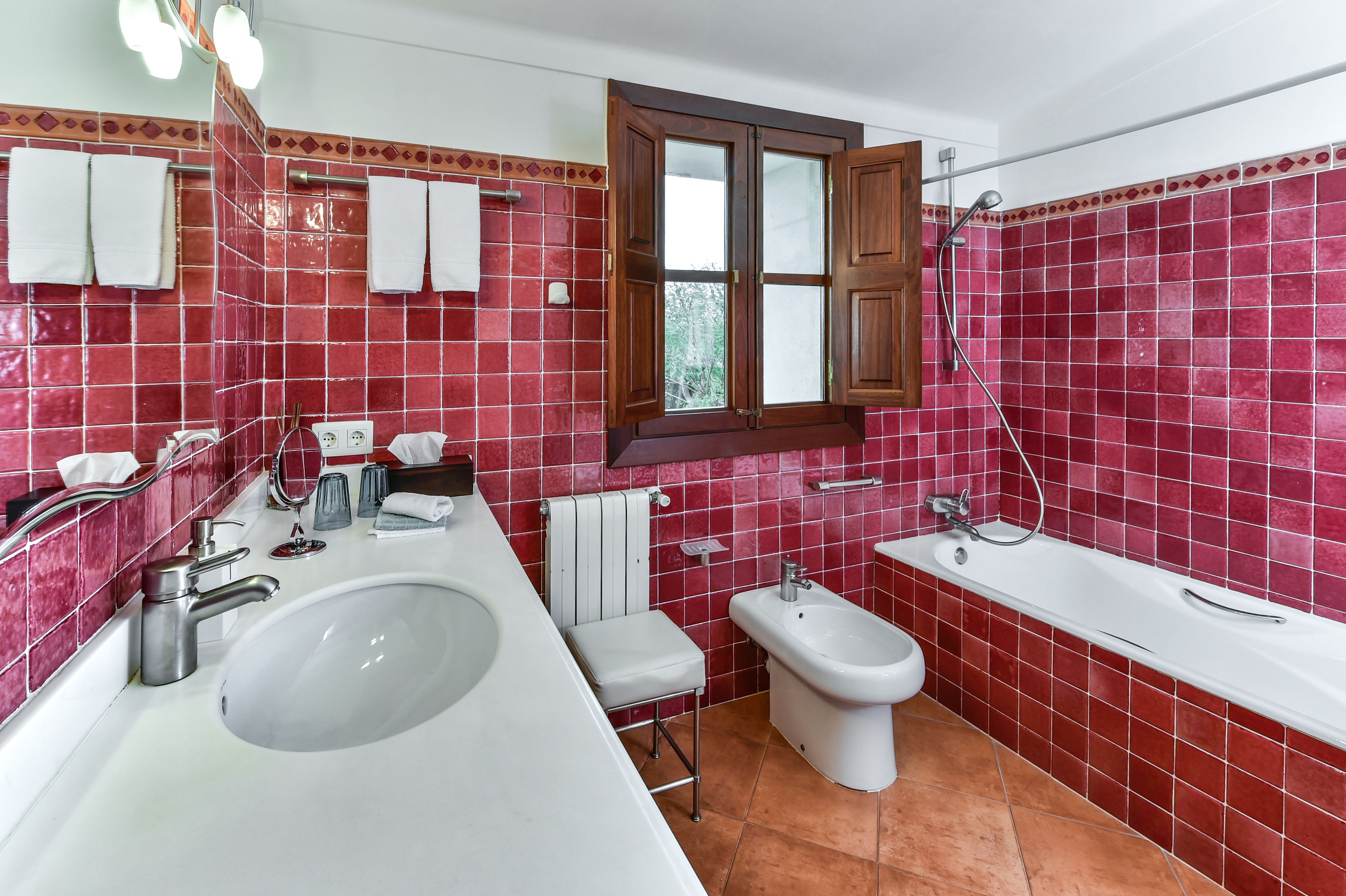 A bathroom with a large white sink, a bidet, a bathtub, and red-tiled walls.