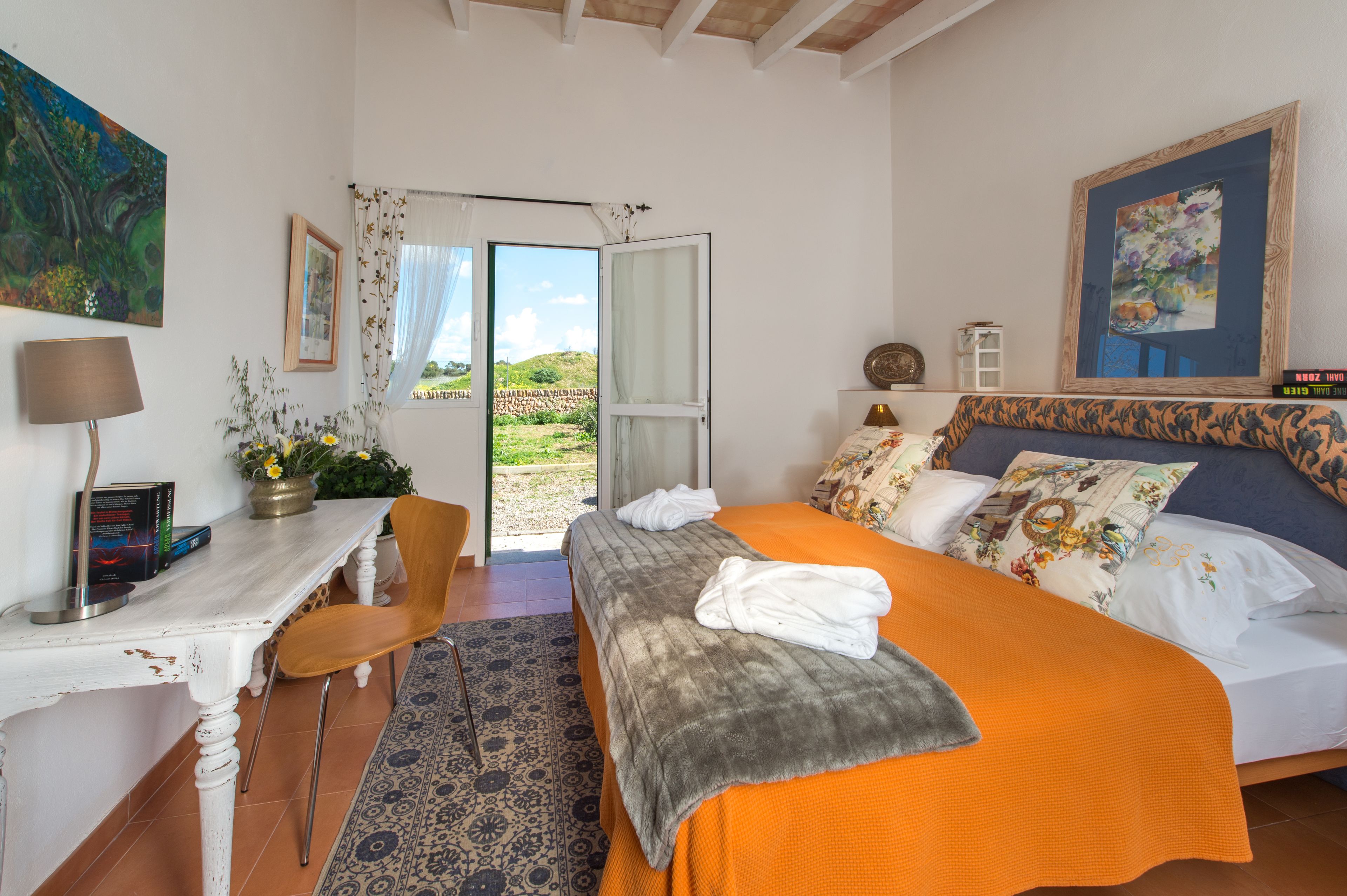 A bedroom with a bed, a desk, a chair, a window, and a door leading outside.