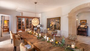 A long wooden dining table set with candles, glass bottles, and greenery, surrounded by patterned chairs in a room with a large painting and a piano. - Agroturismo Fincahotel Es Llobets - Adults Only (Llucmajor)