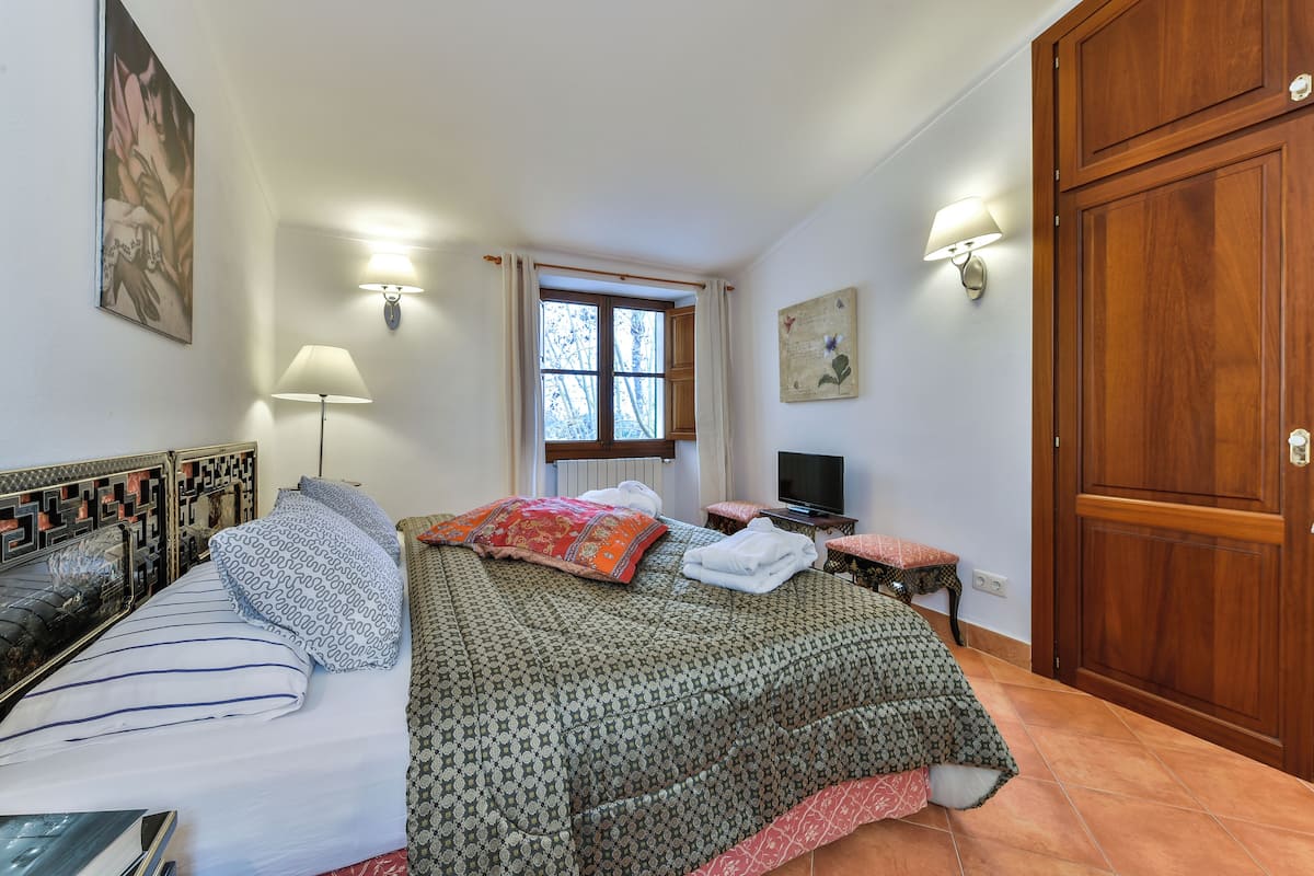 A bedroom with a bed, bedside tables, a TV, a window with curtains, and a wardrobe.