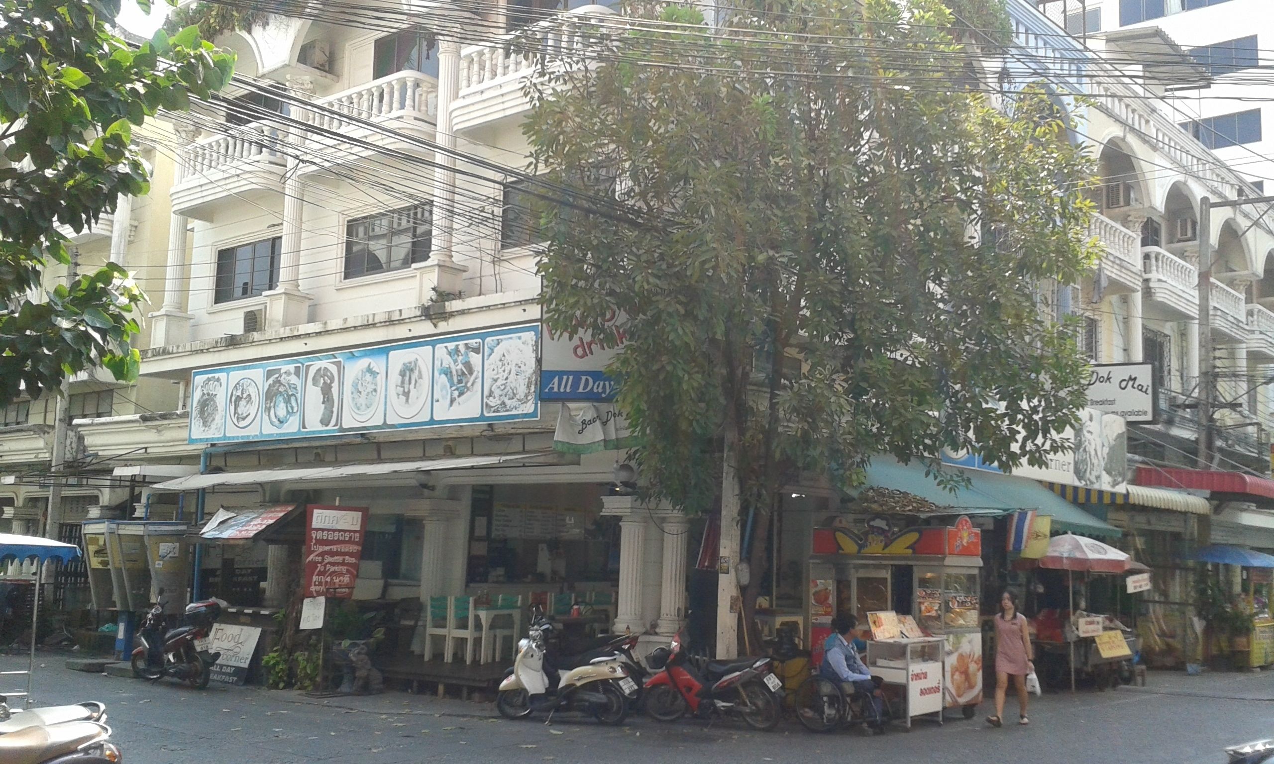 A street scene with parked scooters, a tree, and buildings with signs.