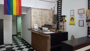 Un espace d’accueil doté d’un sol à carreaux, d’un comptoir de réception, d’un ventilateur de plafond et d’un mur orné d’un motif floral.