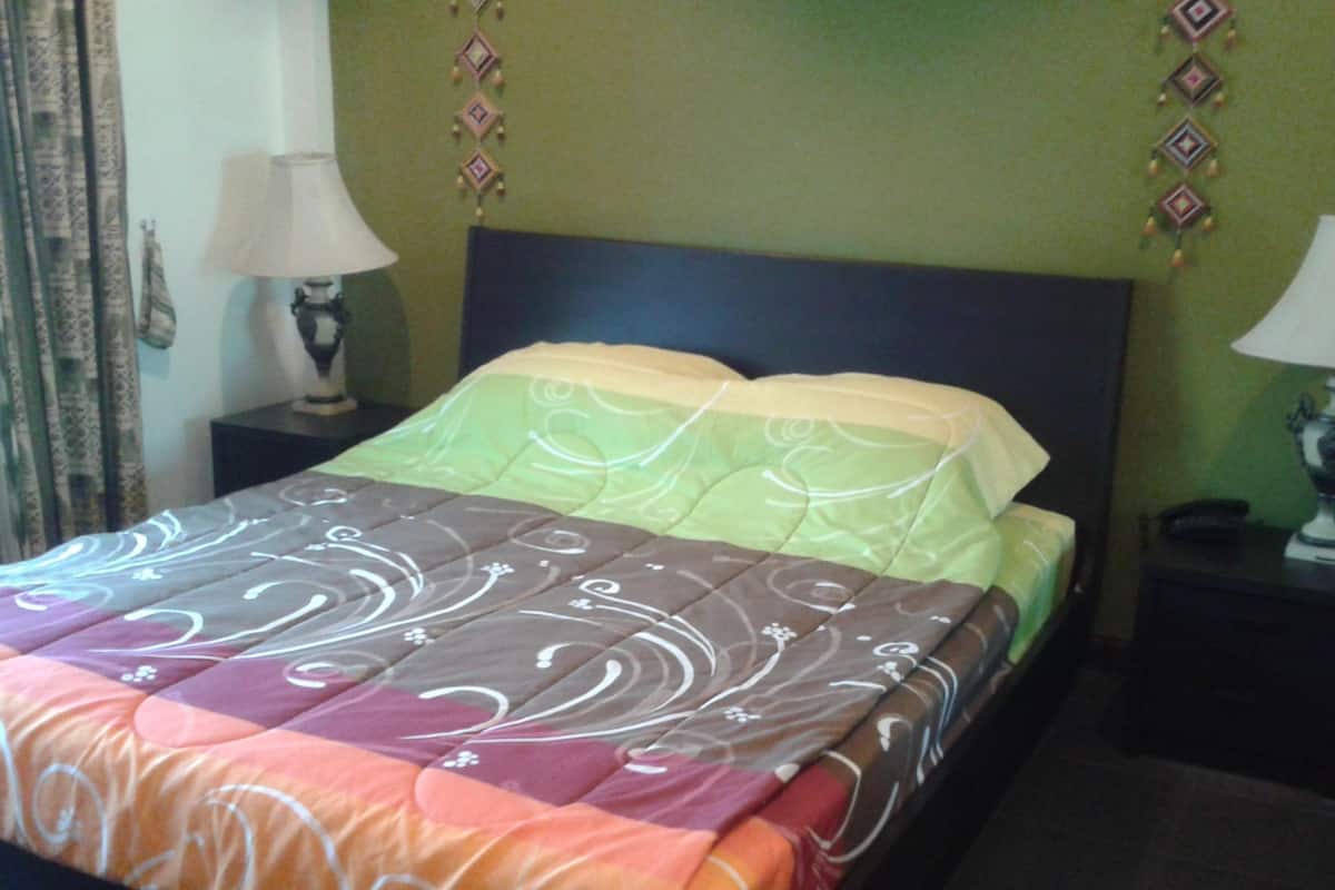 Un lit bien fait, recouvert d’une couvre-lit à motifs, avec deux lampes de chevet et des décorations murales.