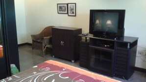 Une chambre d’hôtel avec un téléviseur posé sur un meuble, une armoire, une chaise et deux tableaux encadrés accrochés au mur.