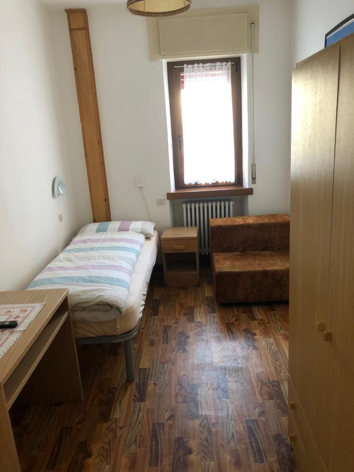 Ein kleiner, kompakter Raum mit Bett, einer Holzbank, einem Schreibtisch und einer Heizung.