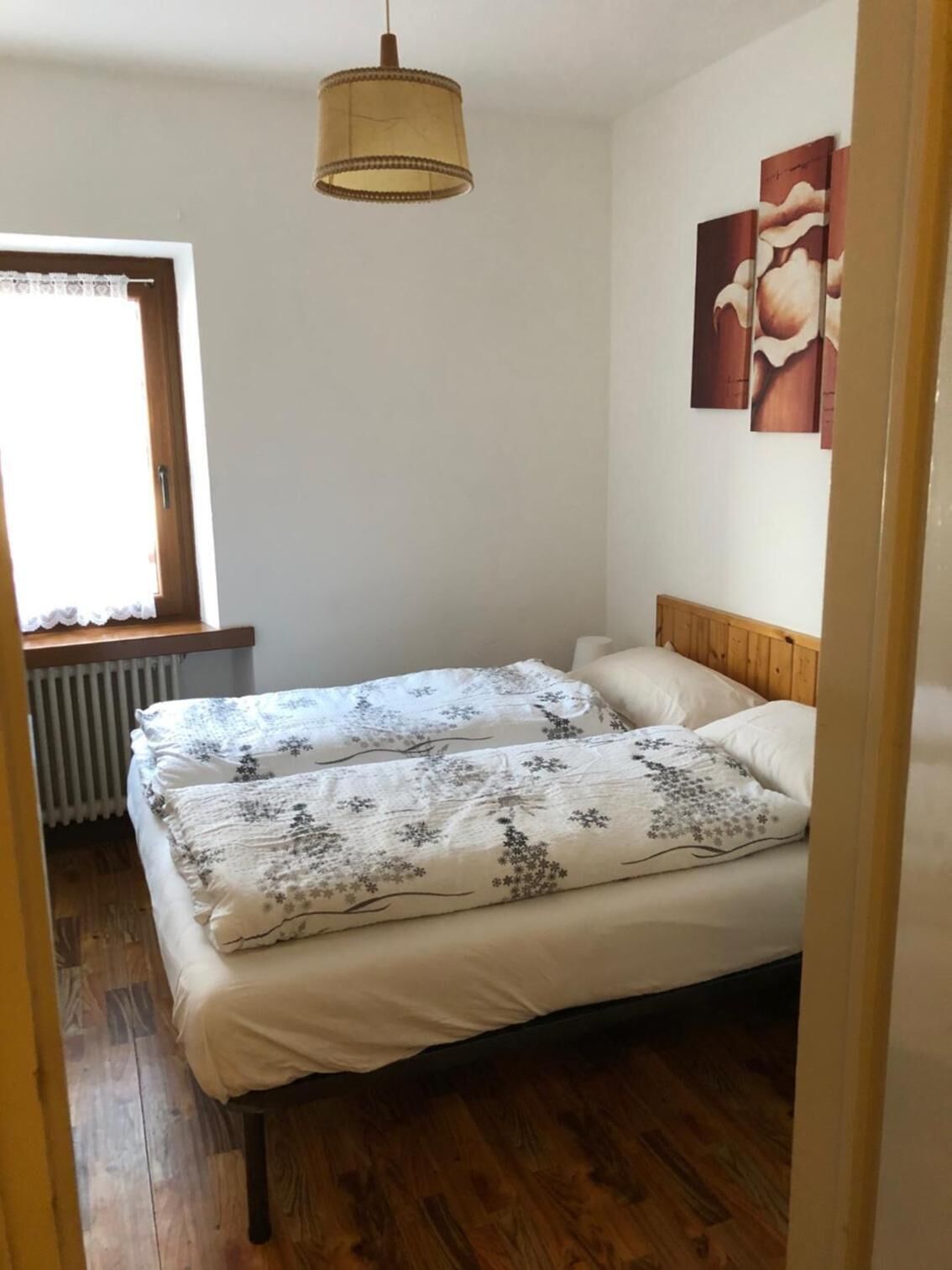 A bedroom with a bed, a window with curtains, a radiator, and a wall-mounted artwork.