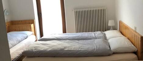 A room with a bed, a radiator, a wooden headboard, a small table with a lace tablecloth, and a wall with abstract art.