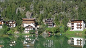 A lakeside hotel with traditional architecture, featuring multiple balconies and a reflection in the water. - Garnì Astor (Alleghe)