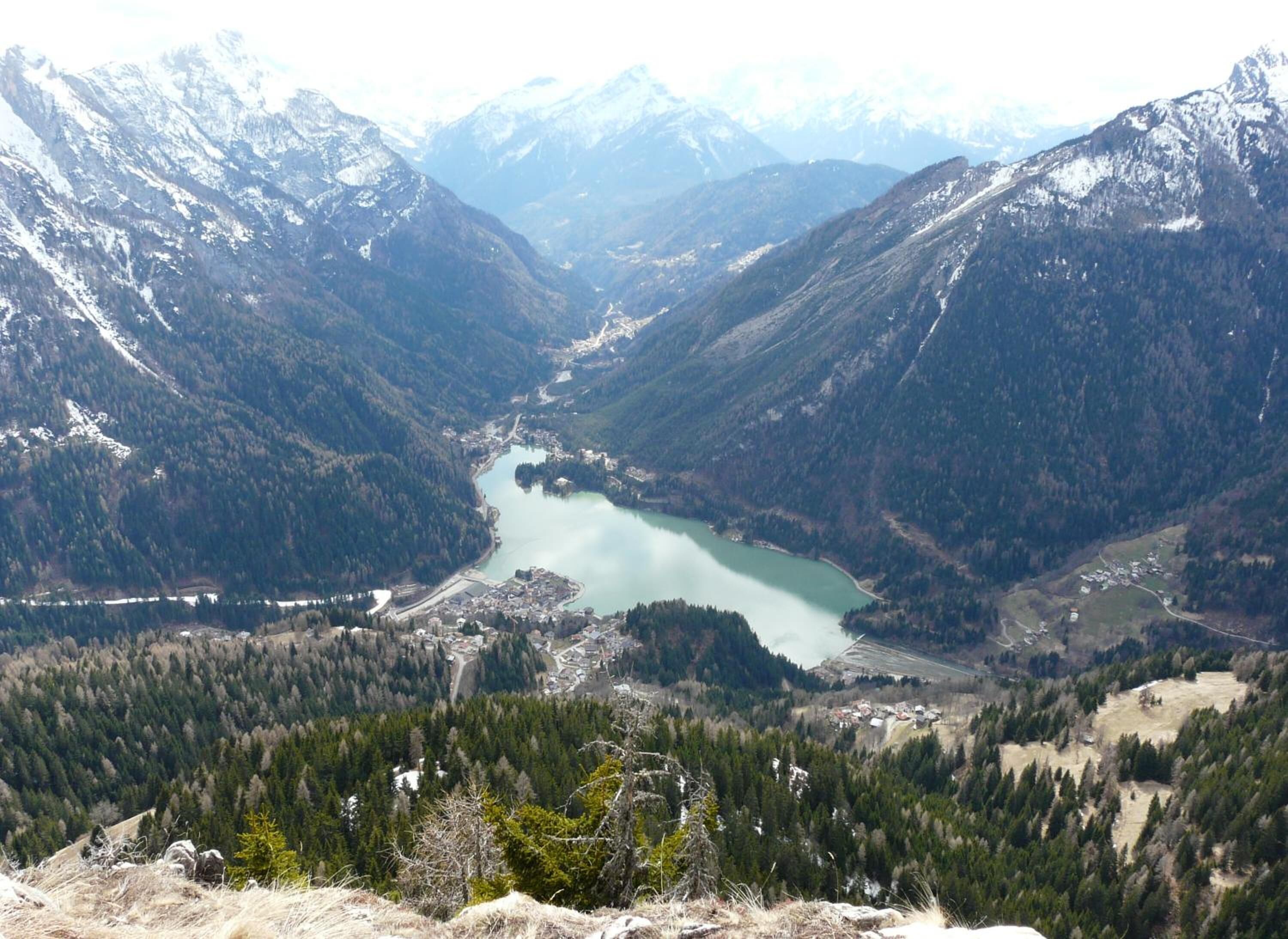A mountainous landscape with a lake surrounded by forested areas and snow-capped peaks.