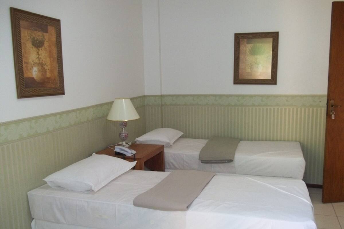 Ein Hotelzimmer mit zwei Betten, einem Nachttisch mit Lampe und zwei gerahmten Bildern an den Wänden.