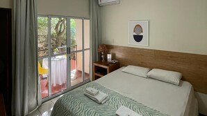 Une chambre d’hôtel avec un lit, une table de chevet, une lampe, un tableau encadré et une fenêtre avec des rideaux.