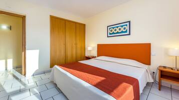 A hotel room with a bed, a wooden wardrobe, a nightstand, and a wall-mounted picture.