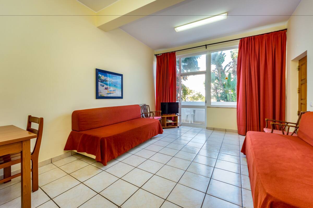 A room with a sofa, a TV, a table, and a chair.