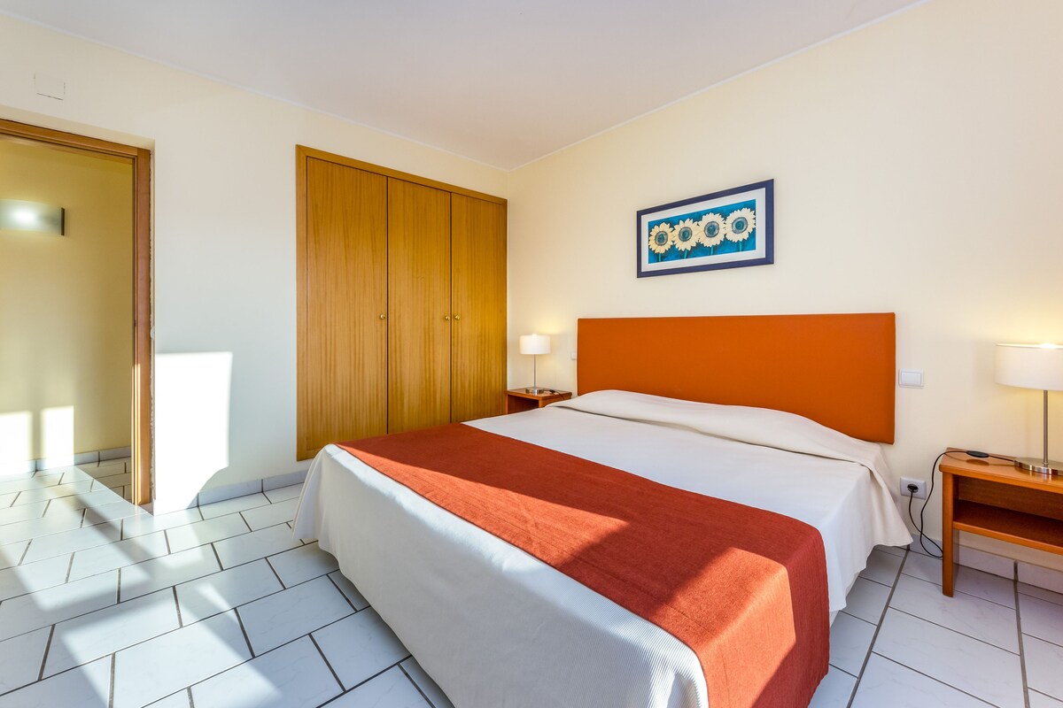 Une chambre d’hôtel avec un lit, une armoire en bois, une table de chevet et un tableau accroché au mur.