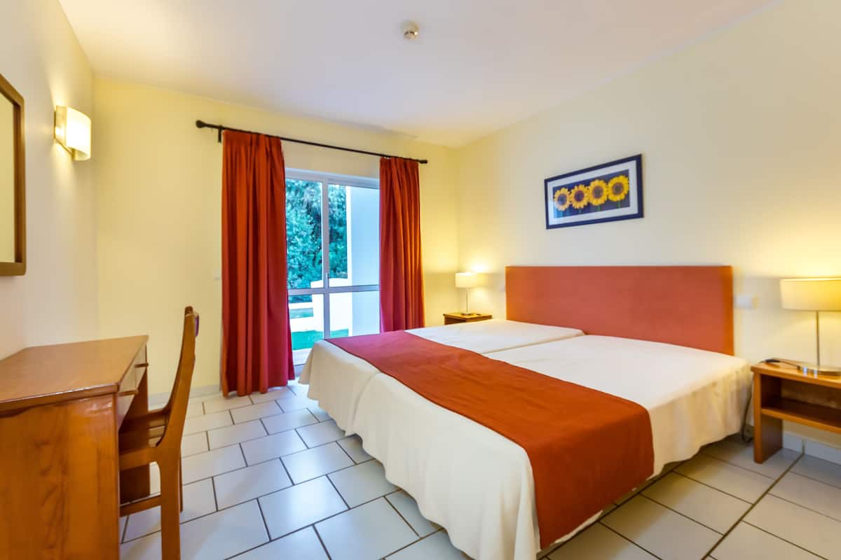 A hotel room with a large bed, a desk, a chair, and a window with curtains.