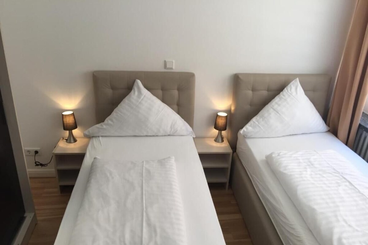 A hotel room with two single beds, each with a headboard, bedside tables, and lamps.