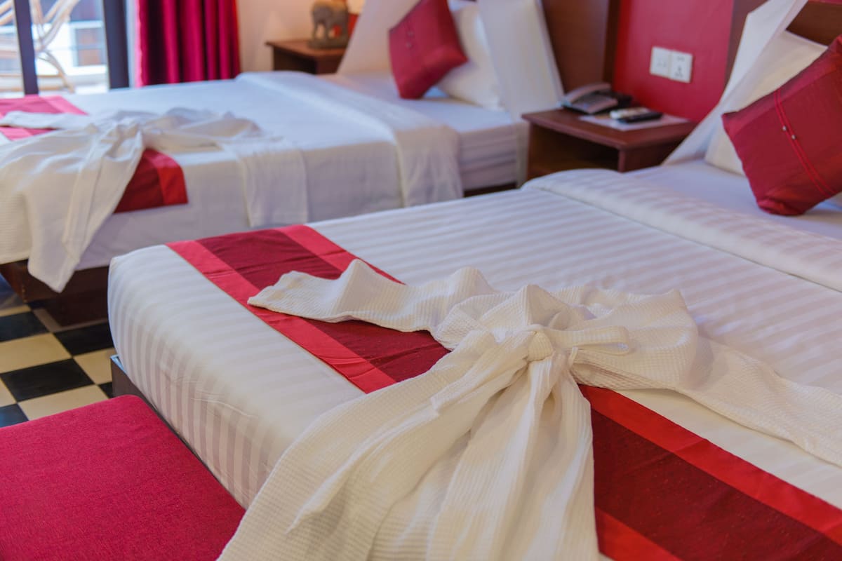 Een hotelkamer met twee bedden, elk voorzien van witte lakens en rode accenten, en een geruite vloer.