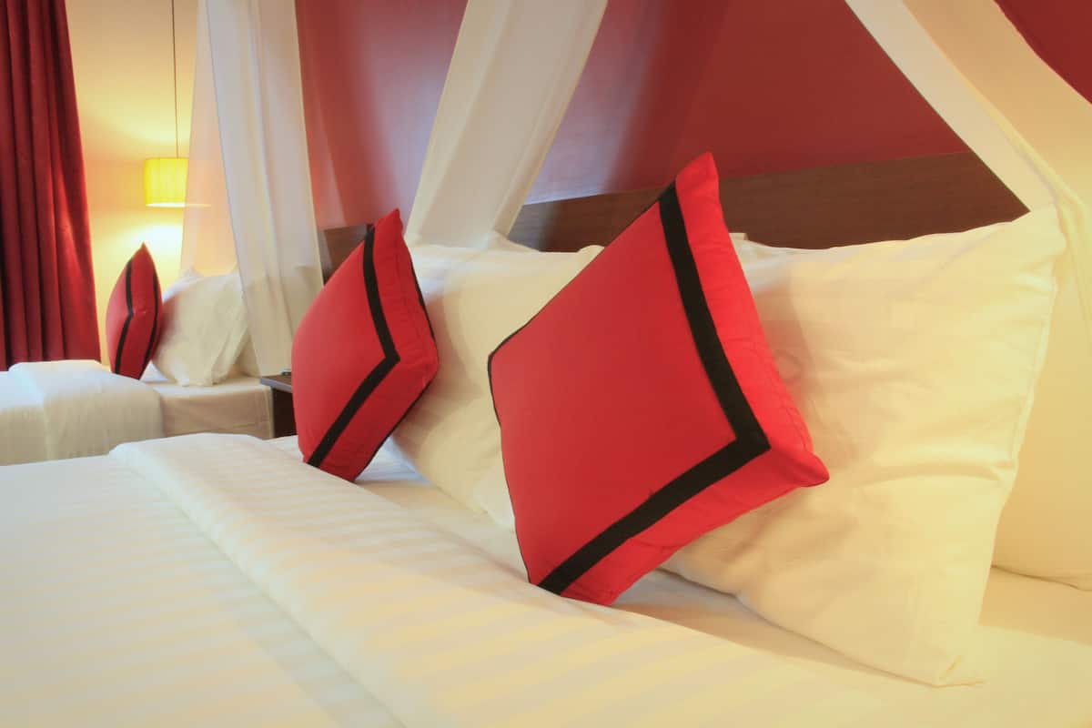 Een hotelkamer met een bed, rode en witte kussens, een nachtkastje en een lamp.