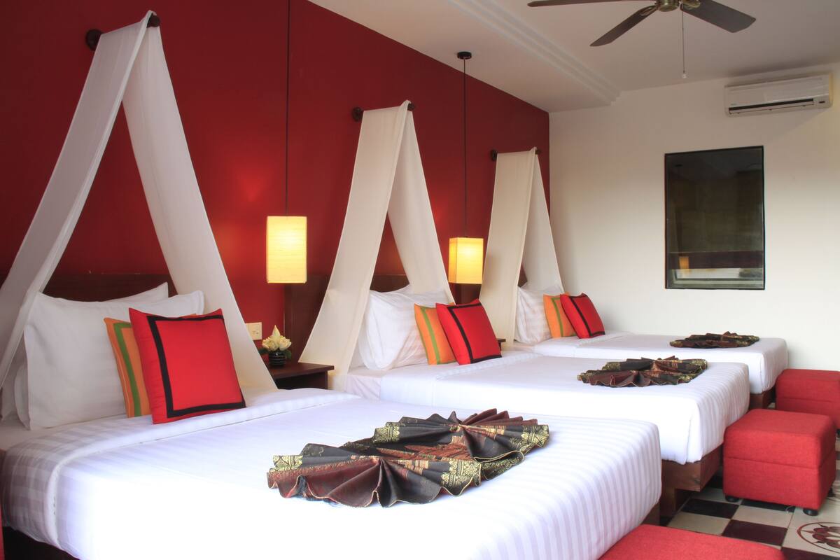 Een hotelkamer met vier bedden, elk voorzien van een hemelbed, rode en witte beddengoed en een geruite vloer.