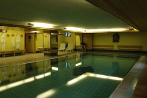 An indoor swimming pool with tiled walls, benches, and a ladder. - Hotel Venezia (Rocca Pietore)