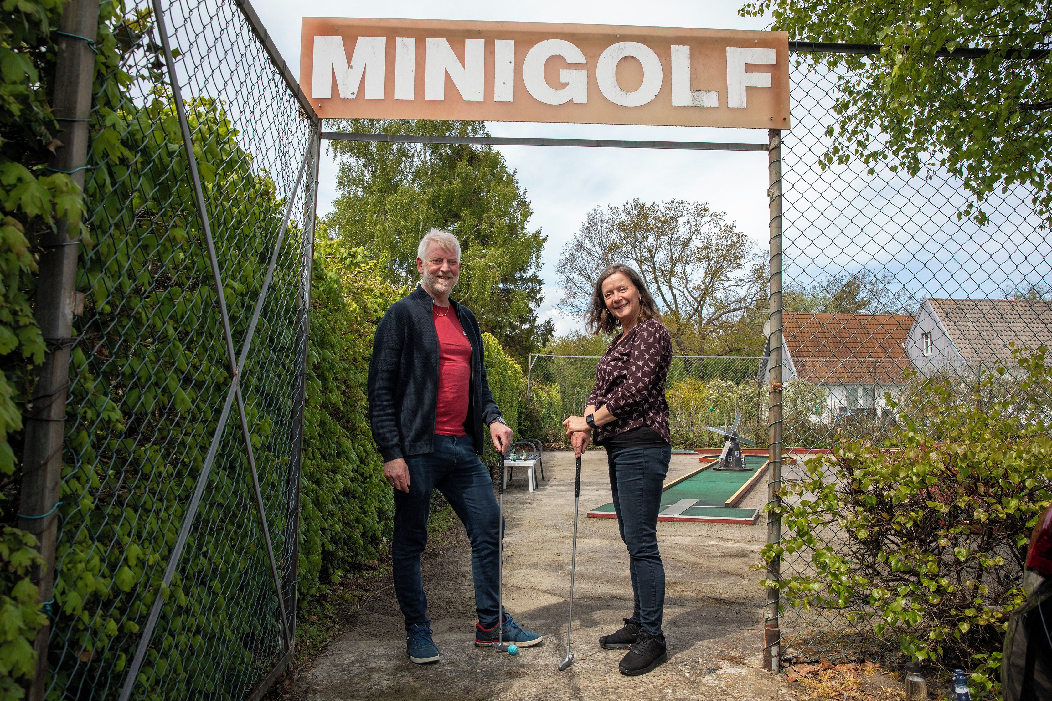 A chain-link fence with a sign that reads 'MINIGOLF' and a golf course visible in the background.