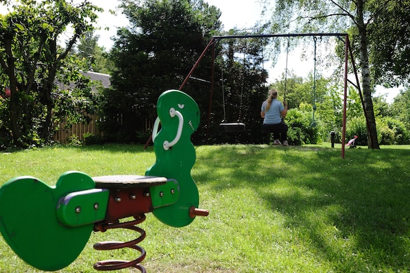 Ein Spielplatz mit einer schwingenden Herzchen-Schaukel und einer weiteren Schaukel in einer grünen Wiese.
