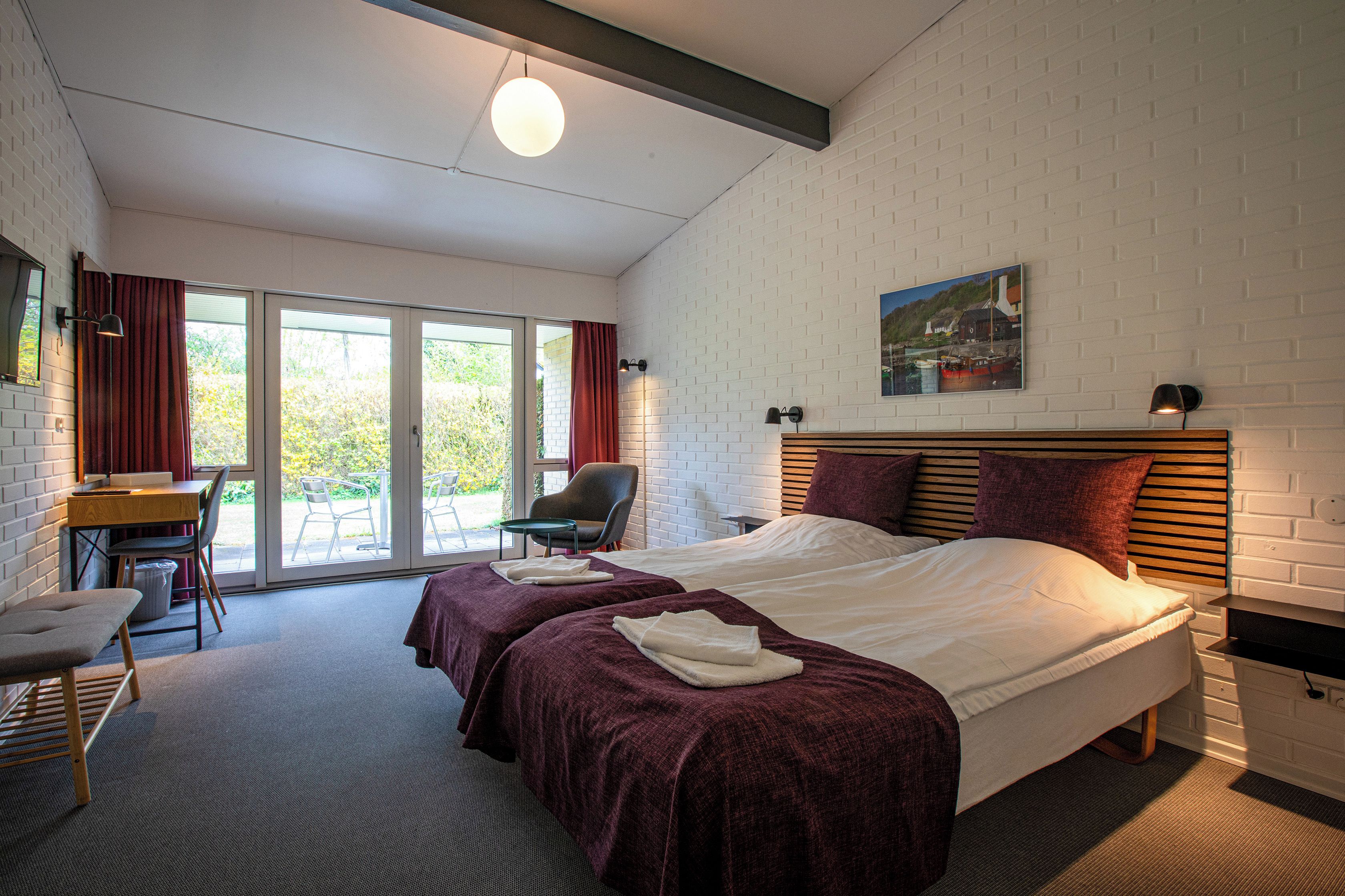 A hotel room with a bed, a desk, a chair, and a view through a glass door.