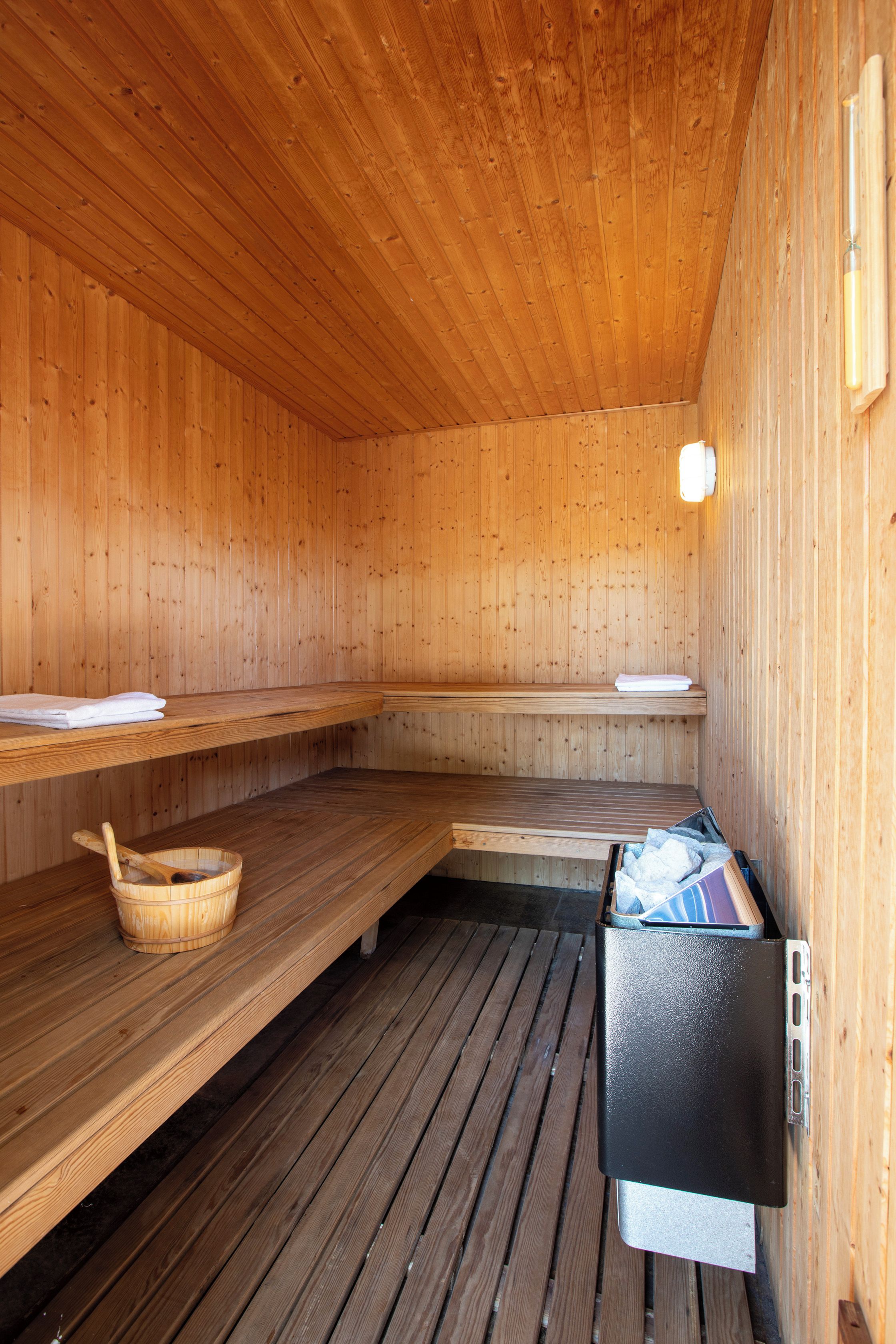 Un sauna avec des murs et des bancs en bois, un plancher en bois et un appareil de chauffage pour sauna.