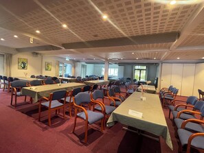 Sala de conferência com várias mesas e cadeiras, uma placa de identificação e uma janela grande.