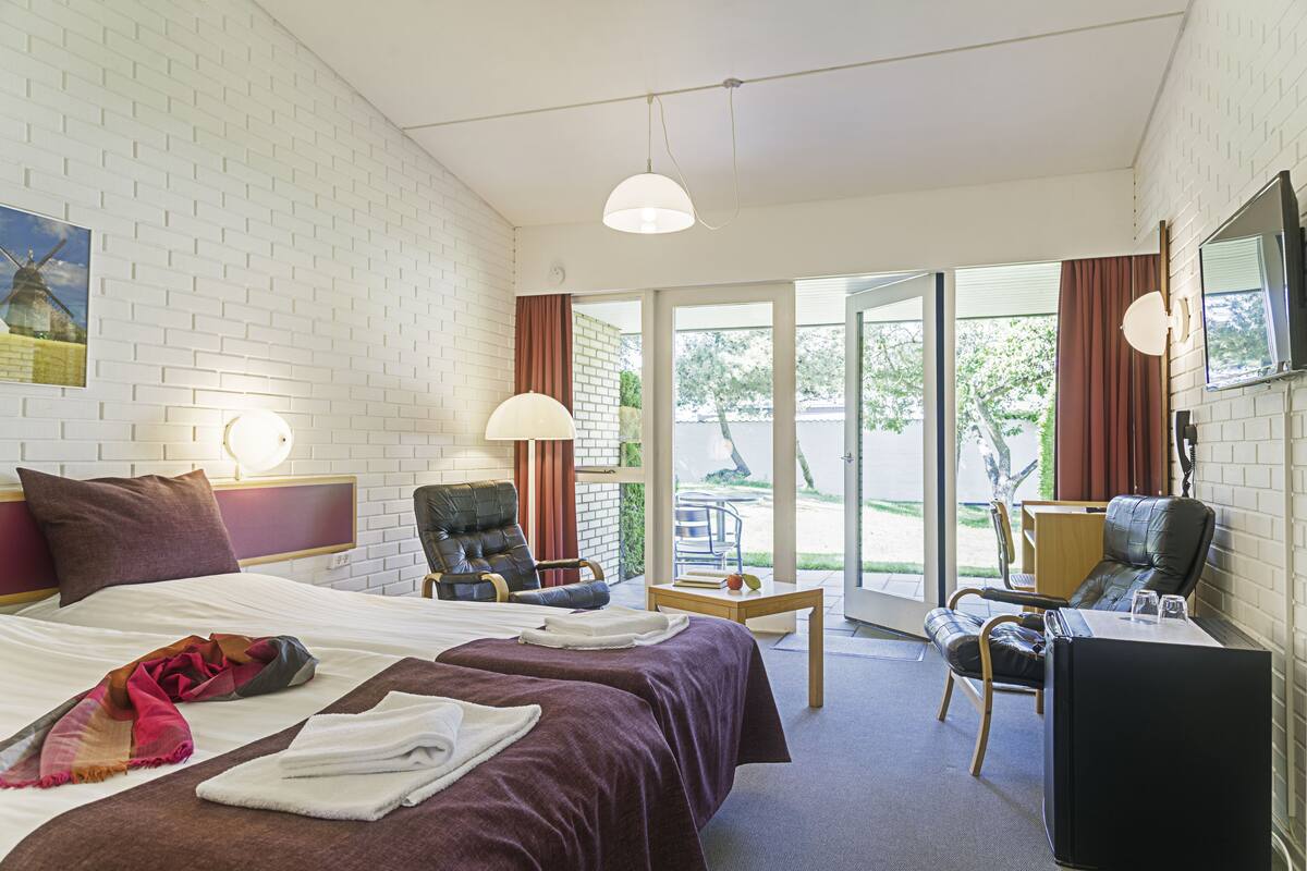 Une chambre d’hôtel avec un lit, deux chaises, un bureau et un téléviseur.