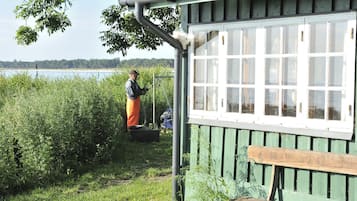 Un edificio de madera rústico con un banco, rodeado de abundante follaje y una masa de agua al fondo.