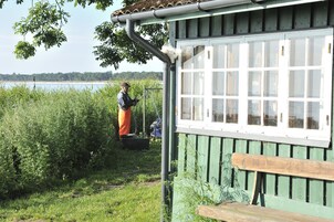Un edificio in legno rustico con una panchina, circondato da vegetazione rigogliosa e uno specchio d'acqua sullo sfondo.