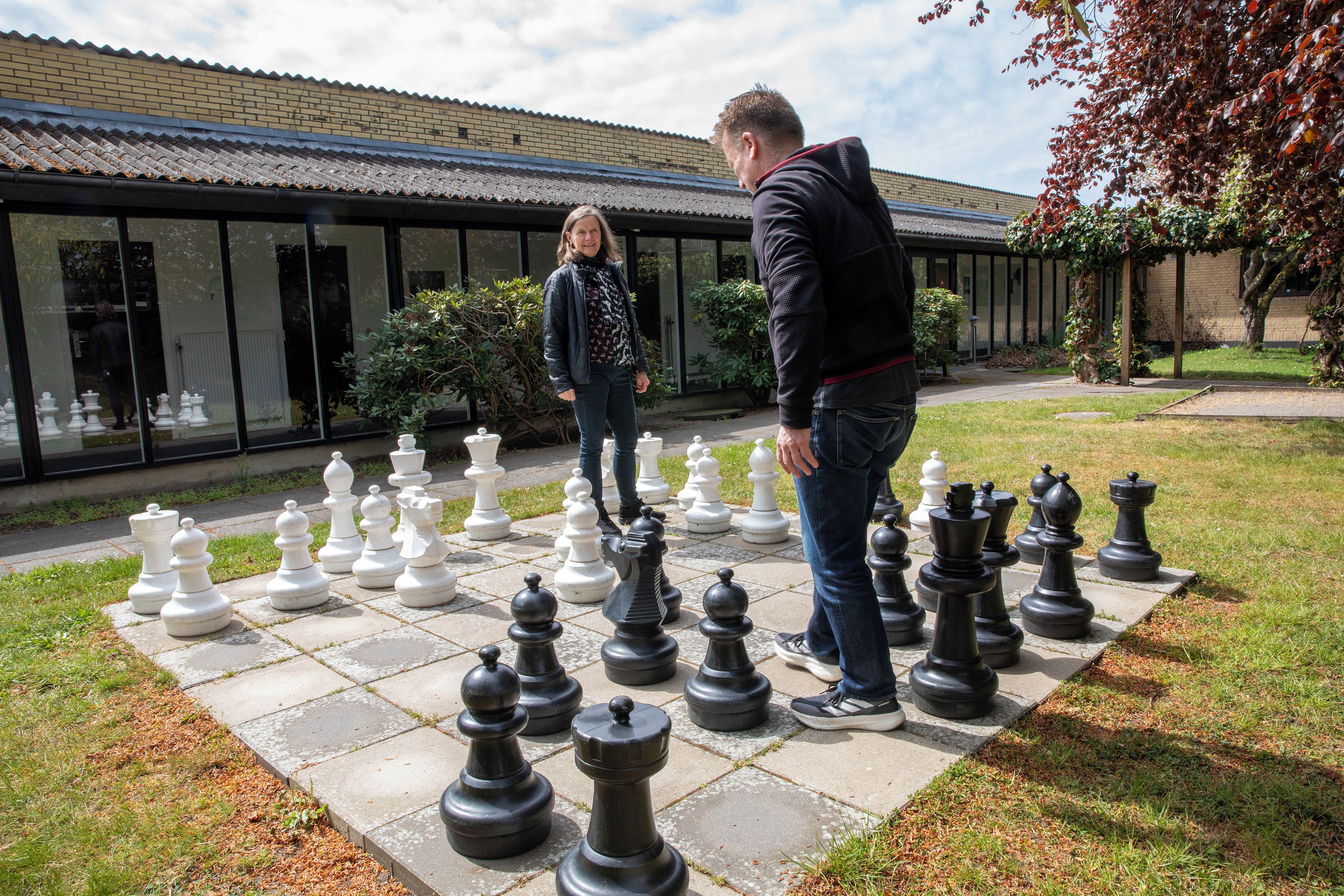 Two people standing on a paved area with a large chessboard setup.