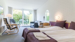 Quarto de hotel com duas camas, uma escrivaninha, uma cadeira e vista para o exterior.