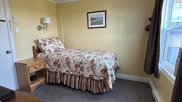 A bedroom with a bed, a nightstand, a lamp, a framed picture on the wall, and a window with curtains.