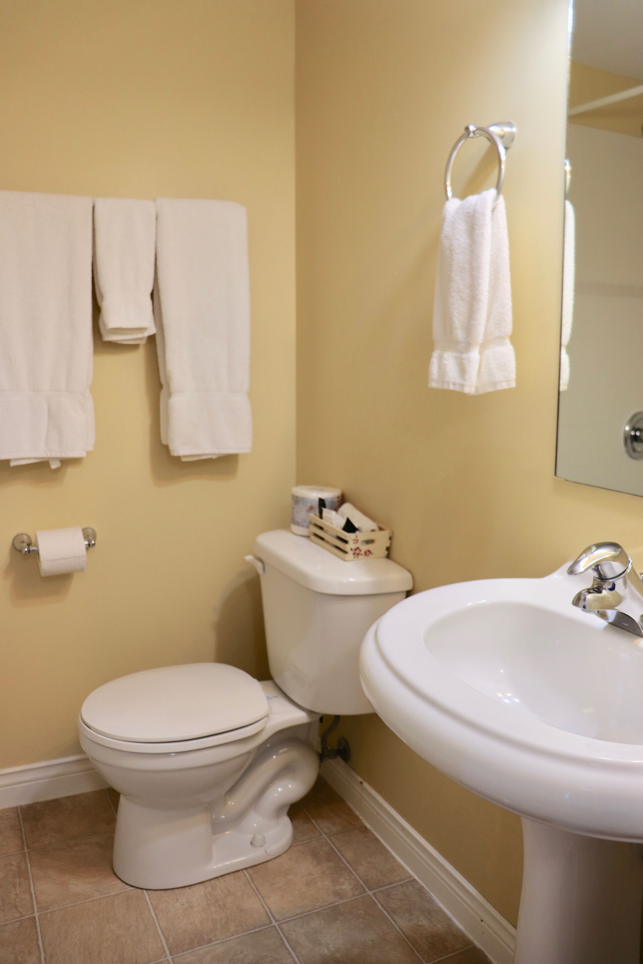 A bathroom with a toilet, sink, and multiple towels hanging on the wall.