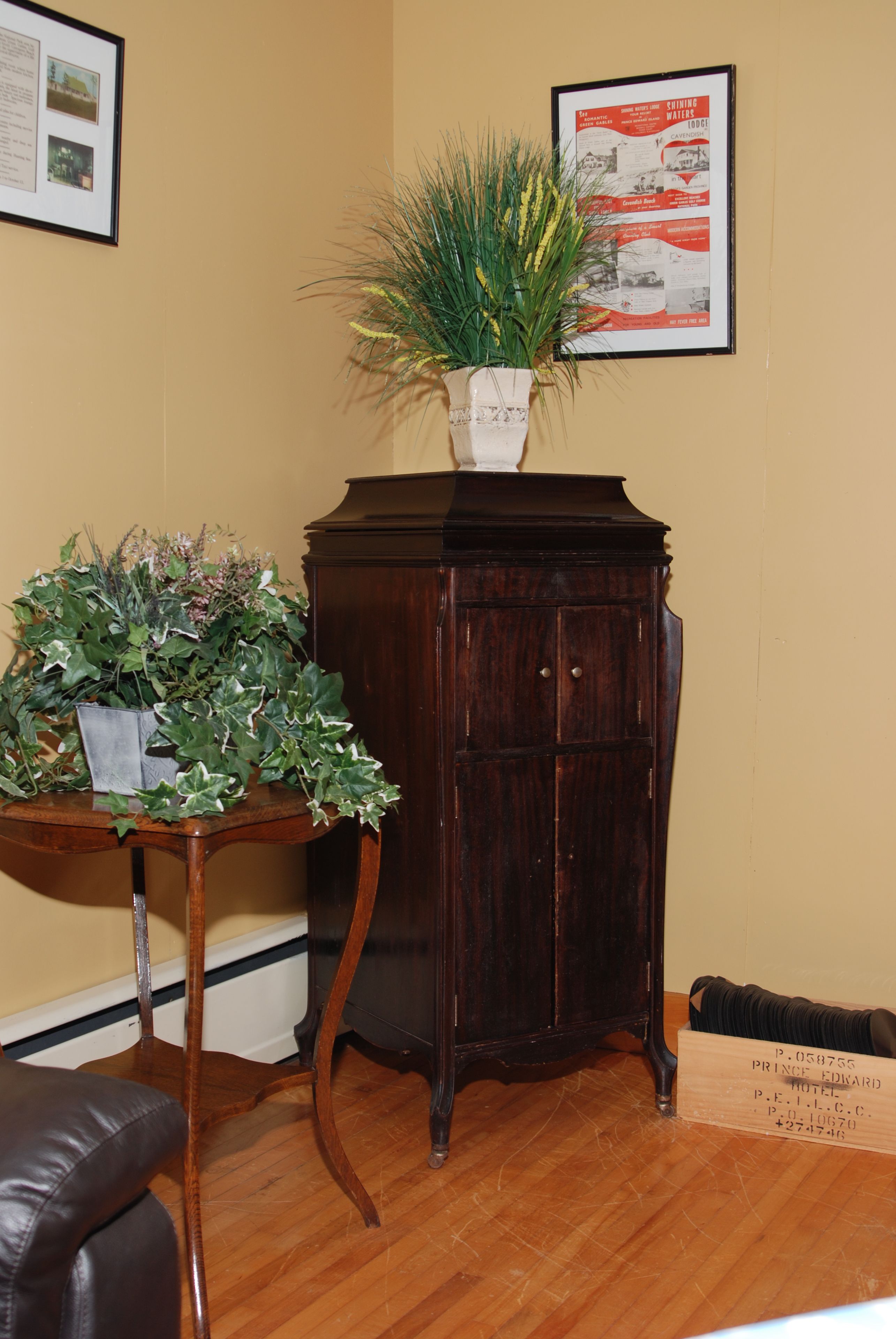 A corner room with a wooden cabinet, a potted plant, and a framed menu on the wall.
